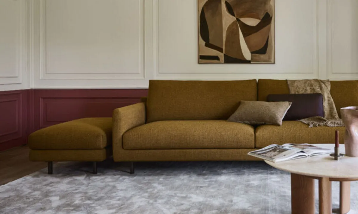 Ockerfarbenes Sofa auf hellem Teppich vor einer Wand mit Bild